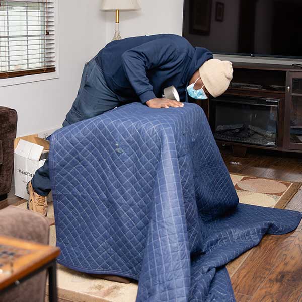 A mover draping a quilted moving blanket over a piece of furniture in a living room