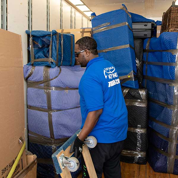 A Gotham mover with a furniture dolly beside stacks of pad-wrapped goods inside a truck