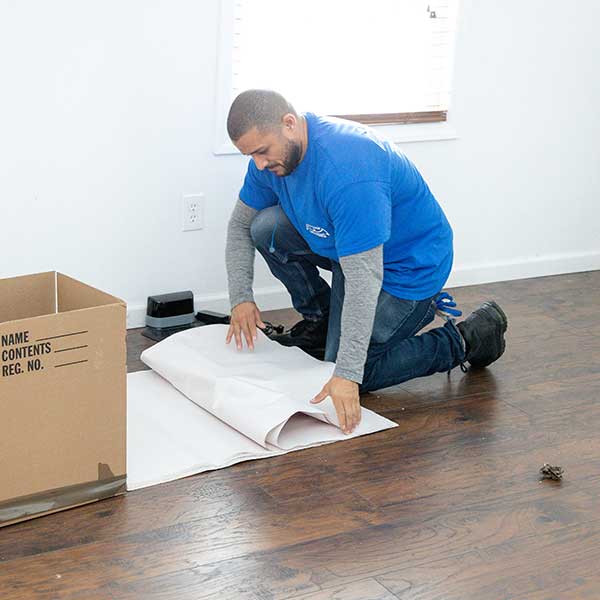 A Gotham mover kneeling to fold packing paper beside a carton