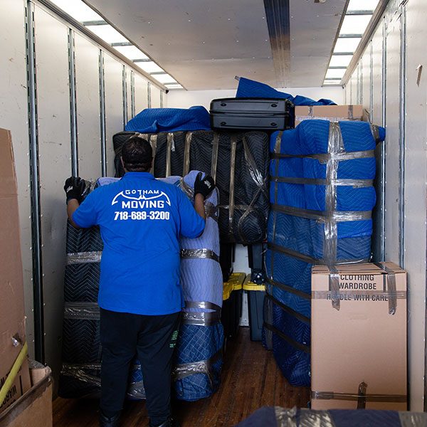 A Gotham mover securing pad-wrapped furniture and wardrobe boxes inside a truck