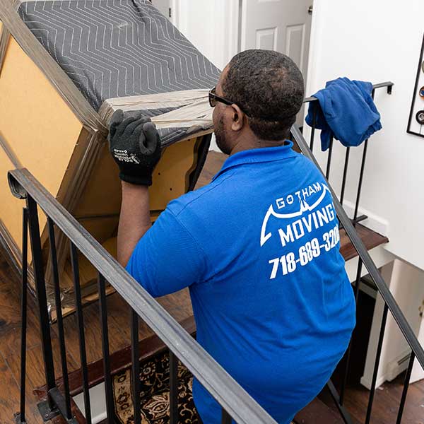 A Gotham mover guiding a pad-wrapped piece down a staircase past an iron rail