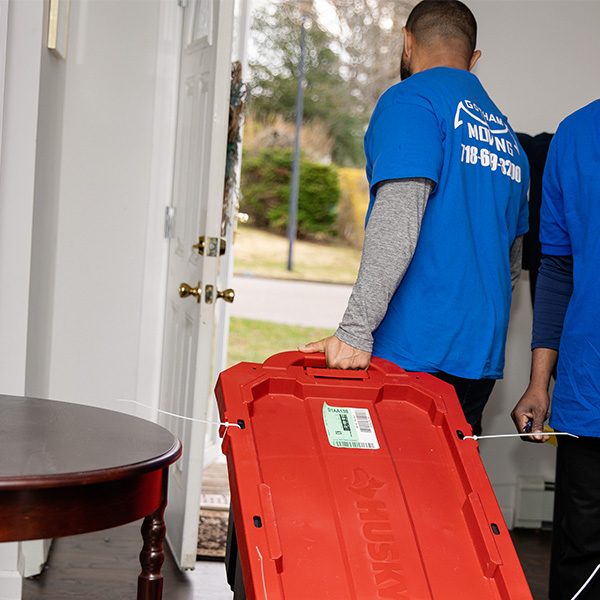 Gotham movers carrying a red tote through a front doorway past a side table