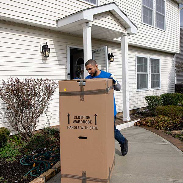 A Gotham mover wheeling a tall wardrobe box out of a front door