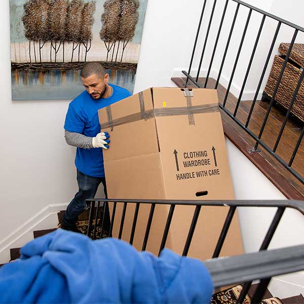 A Gotham mover carrying a wardrobe box up a staircase past an iron rail