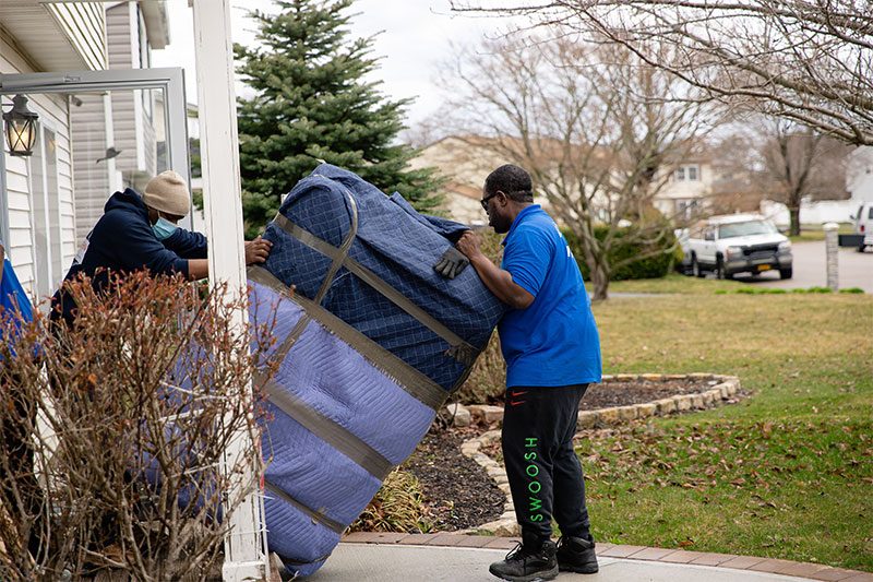 Two movers tilting a large pad-wrapped piece through a front porch