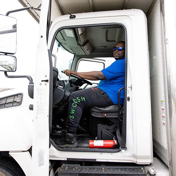 A Gotham driver at the wheel of a box truck, cab door open