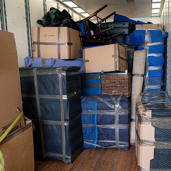 A fully packed truck: pad-wrapped furniture, cartons, a rug roll and chairs stacked to the roof