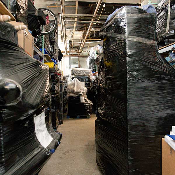 A narrow warehouse aisle between tall shrink-wrapped stacks
